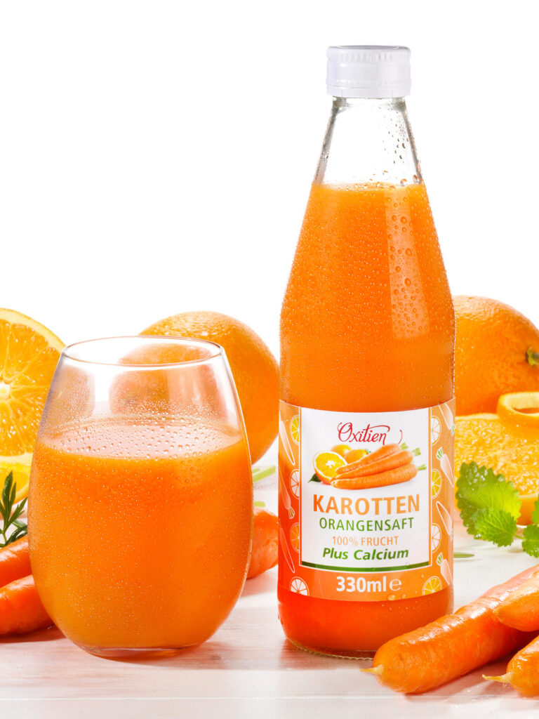 Karotten-Orangensaft von Oxitien mit Glas und Orangen sowie Karotten